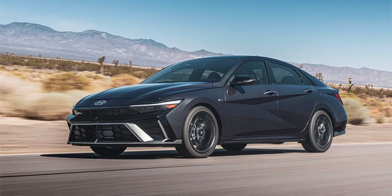 Dark gray Hyundai Elantra N Line driving on a desert road with mountains in the background.