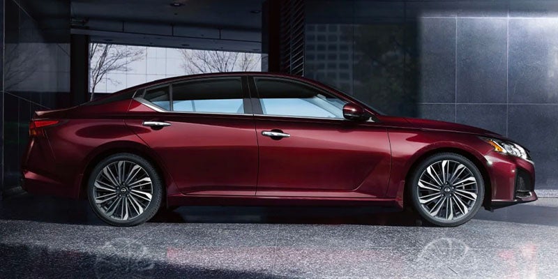 Side view of a dark red sedan with chrome accents, parked on a reflective surface against a modern building.