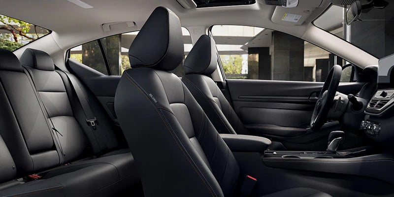 Interior view of a car, showing black leather seats, dashboard, and steering wheel, with natural light from outside.