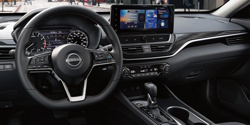 Interior view of a Nissan car with a black steering wheel, dashboard, gear shift, and a large display screen.