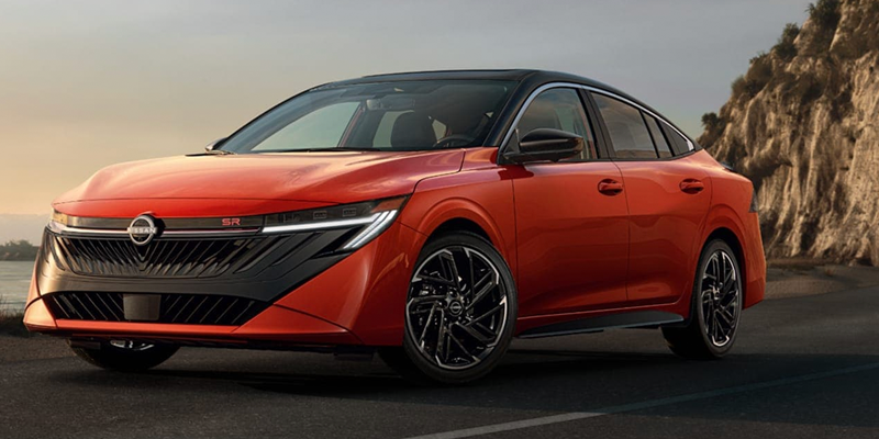 A sleek orange car with a black roof and black grille is parked on an asphalt road next to a rocky cliff.